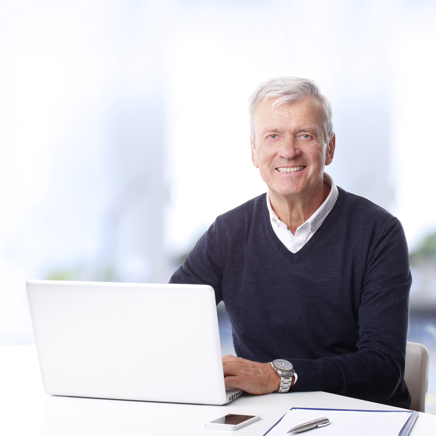 Close-up portrait of handsome senior businessman using a laptop while looking at camera.